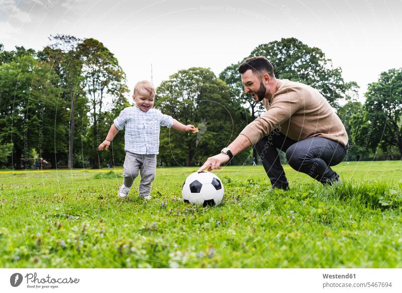 Happy father playing football with son in a park active happiness happy parks soccer fathers daddy dads papa sons manchild manchildren Activity sport sports