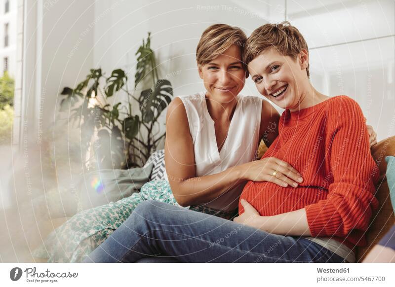 Portrait of happy lesbian couple touching belly of the expectant mother pregnant Pregnant Woman happiness portrait portraits twosomes partnership couples