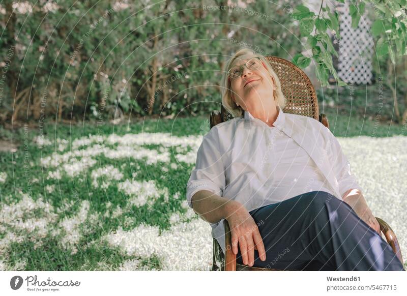 Thoughtful senior woman looking up while relaxing on chair in yard color image colour image Spain leisure activity leisure activities free time leisure time