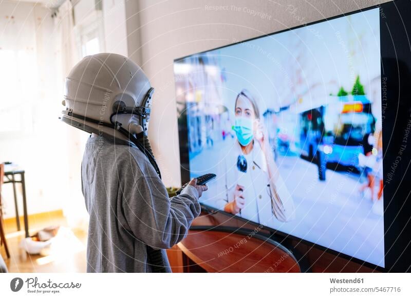 Boy wearing space helmet watching journalist mother on TV while standing at home color image colour image Spain indoors indoor shot indoor shots interior