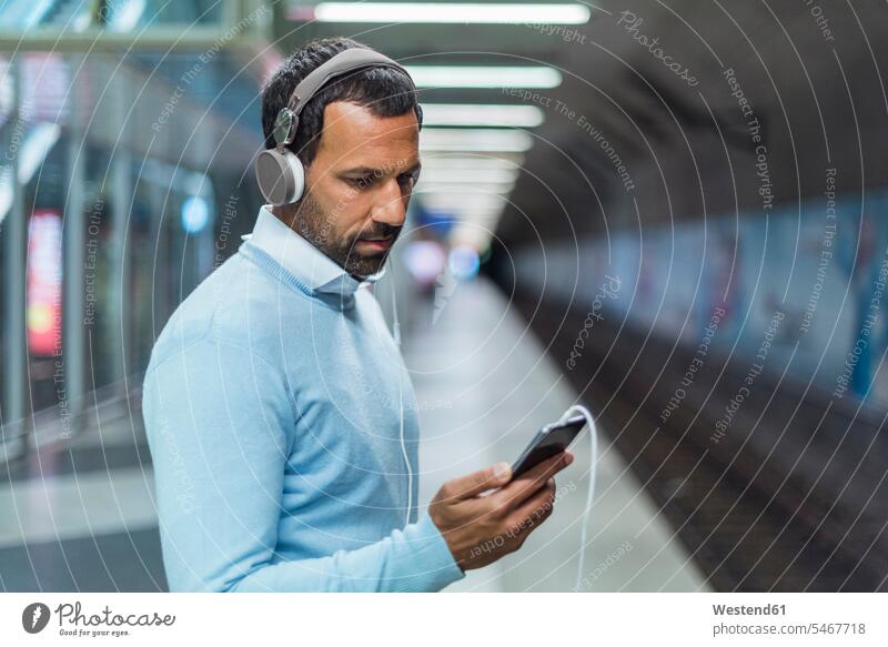 Businessman using smartphone at metro station on the phone call telephoning On The Telephone calling earphones ear phone ear phones portrait portraits hearing