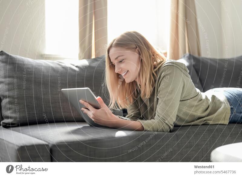 Portrait of smiling young woman lying on the couch at home using digital tablet human human being human beings humans person persons celibate celibates singles