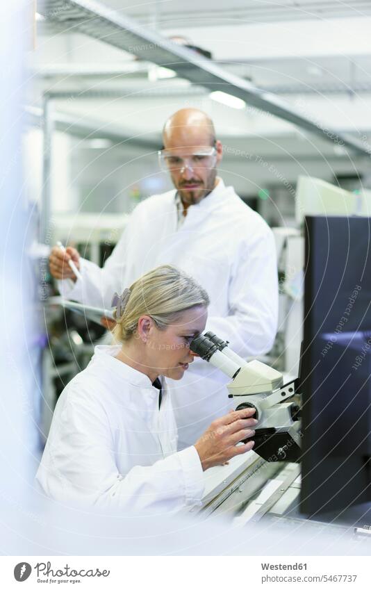 Female scientist doing research while looking into microscope by male colleague in laboratory color image colour image indoors indoor shot indoor shots interior