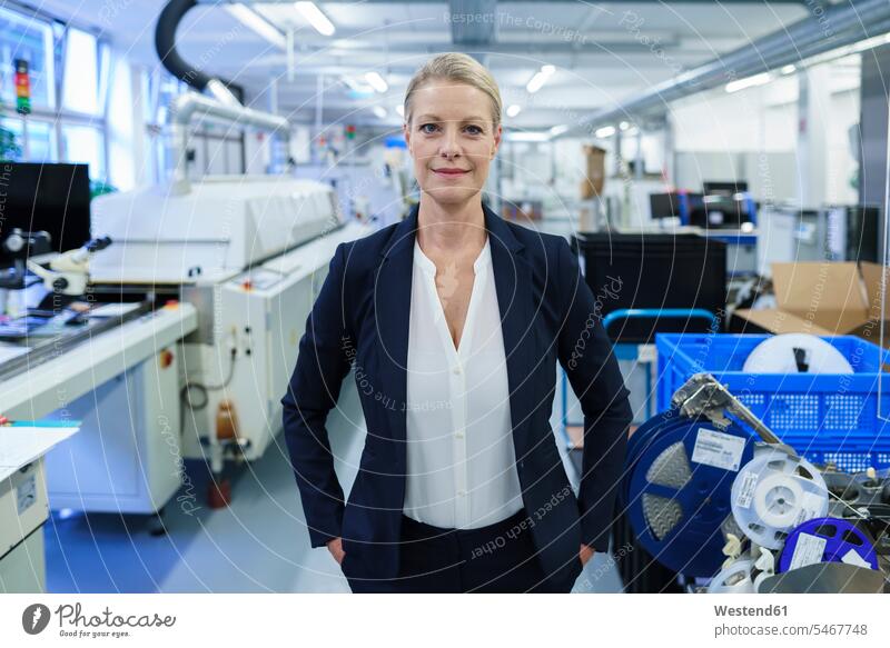 Confident smiling businesswoman standing with hands in pockets in illuminated factory color image colour image indoors indoor shot indoor shots interior