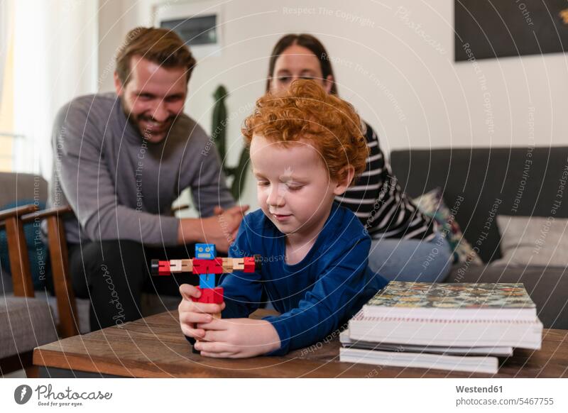 Parents looking at cute son playing with toy robot on table in living room color image colour image leisure activity leisure activities free time leisure time