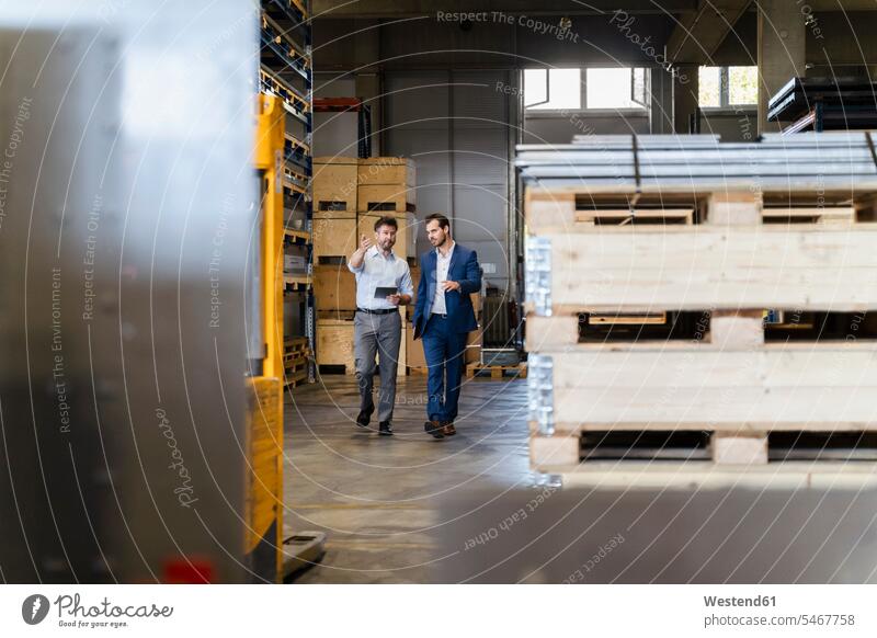 Businessman and colleague inspecting warehouse while walking at factory color image colour image indoors indoor shot indoor shots interior interior view