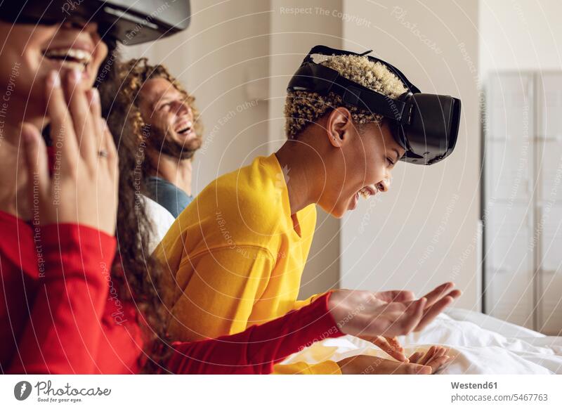 Happy friends having fun with VR glasses in bed at home (value=0) human human being human beings humans person persons Mixed Race mixed race ethnicity
