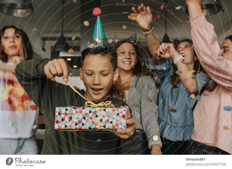 Curious birthday boy opening gift while friends dancing in background color image colour image Germany indoors indoor shot indoor shots interior interior view