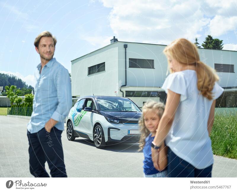 Family with electric car in front of house family families automobile Auto cars motorcars Automobiles houses electric vehicle electric vehicles transportation