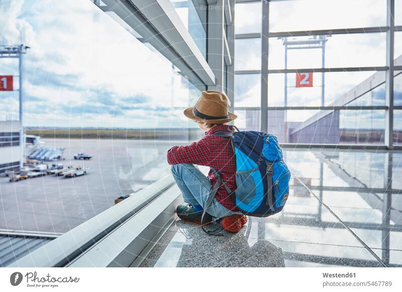 Boy sitting behind windowpane at the airport looking at airfield airports boy boys males Seated view seeing viewing windows window glass window glasses