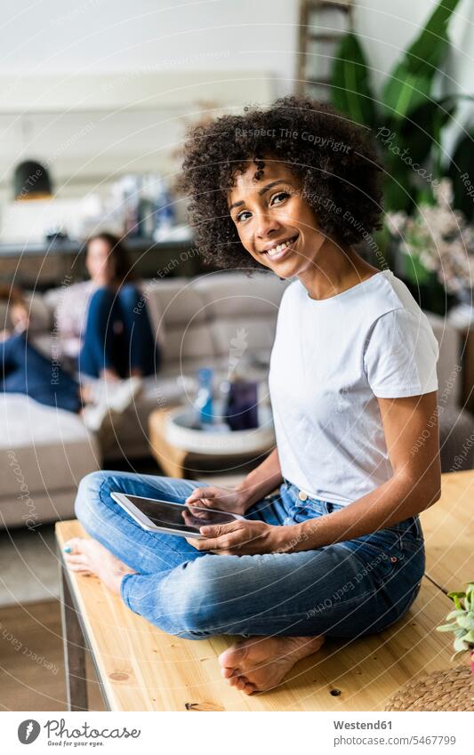Portrait of smiling woman with tablet on table at home with friends in background portrait portraits Table Tables smile female friends sitting Seated females