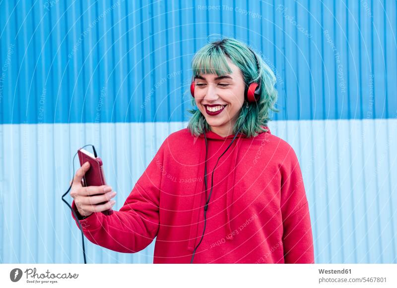 Portrait of laughing young woman with blue dyed hair with headphones taking selfie with mobile phone coloured Smartphone iPhone Smartphones Laughter portrait