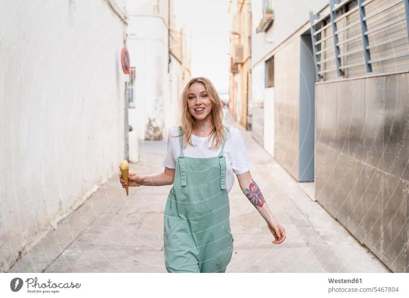 Portrait of happy young woman with ice cream cone walking along an alley human human being human beings humans person persons caucasian appearance