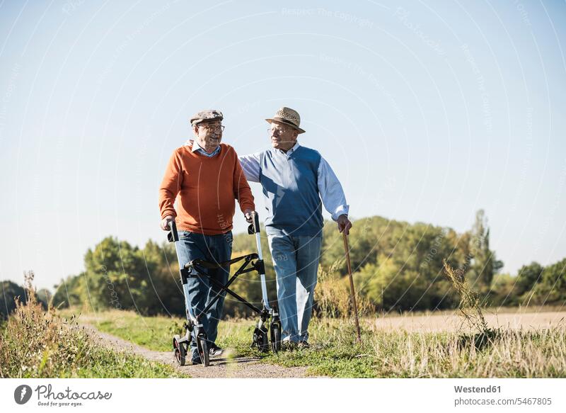 Old friends taking a stroll in the fields with walking stick and wheeled walker, talking about old times Germany Stroll age togetherness familiarity sharing