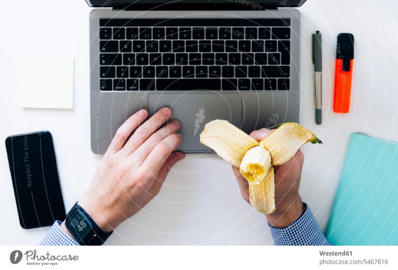 Hands of man typing on laptop and eating banana indoors indoor shot indoor shots interior interior view Interiors elevated view High Angle View High Angle Shot