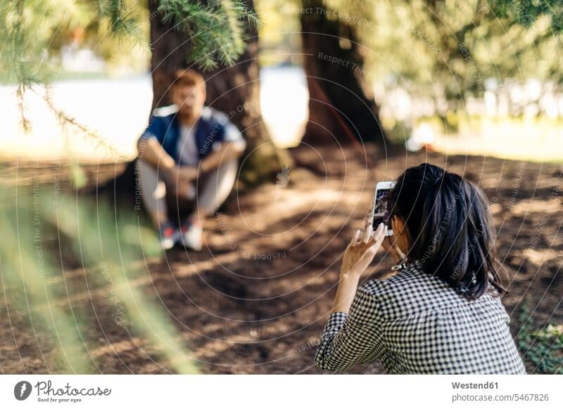 Young woman taking cell phone picture of boyfriend under a tree telecommunication phones telephone telephones cell phones Cellphone mobile mobile phones mobiles