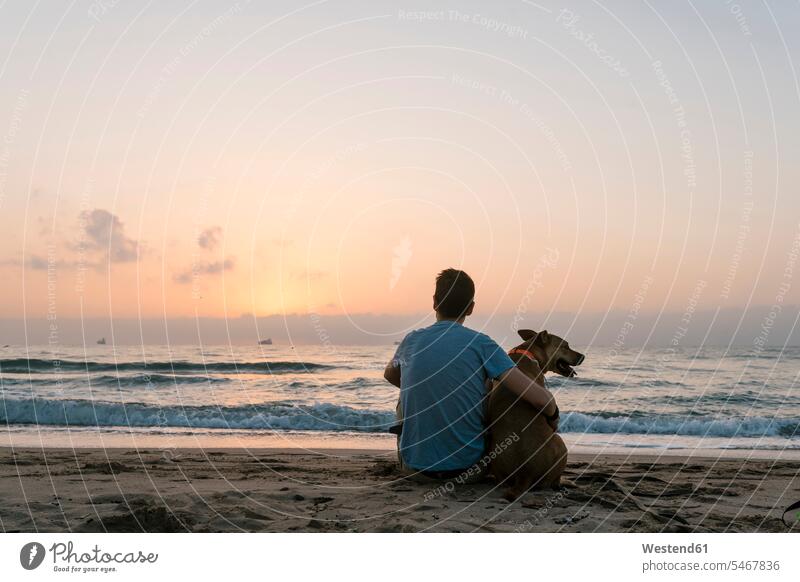 Man sitting with his dog enjoying dawn at beach color image colour image outdoors location shots outdoor shot outdoor shots casual clothing casual wear