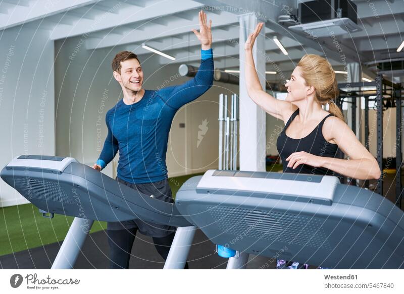 Happy man and woman doing high five during treadmill exercise at gym females women running High Five high fiving Hi-Five high-fiving High-Five Treadmills