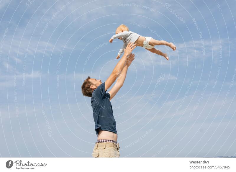 Germany, Timmendorfer Strand, Father throwing son in the air Fun having fun funny sky skies nature natural world exhilaration elation cheerful Trust Confidence