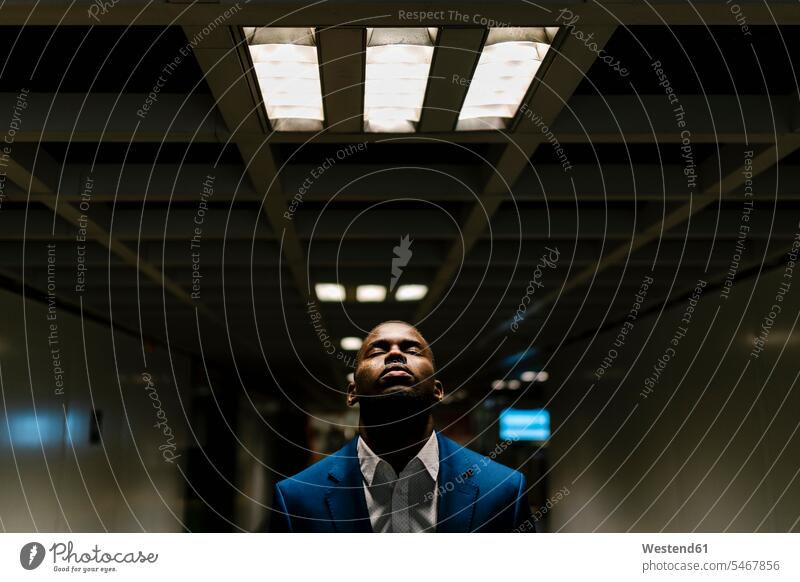 Male professional with eyes closed standing under illuminated light in subway color image colour image Spain Businessman Businessmen Business man Business men