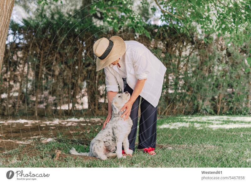 Senior woman wearing hat with dog standing on grassy land in yard color image colour image Spain leisure activity leisure activities free time leisure time