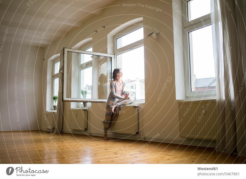 Mature woman in empty room holding tablet looking out of window windows day daylight shot daylight shots day shots daytime females women digitizer