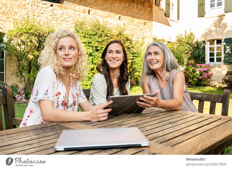Three women of different age sitting at garden table using tablet happiness happy Garden Table Outdoor Table digitizer Tablet Computer Tablet PC