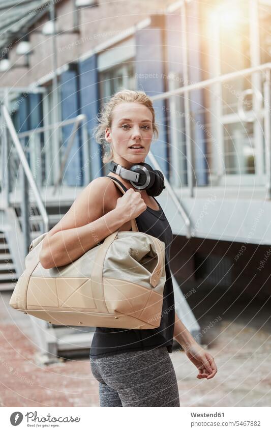 Portrait of blond young woman with headphones and sports bag in front of gym headset portrait portraits Gym Bag gyms Health Club females women blond hair