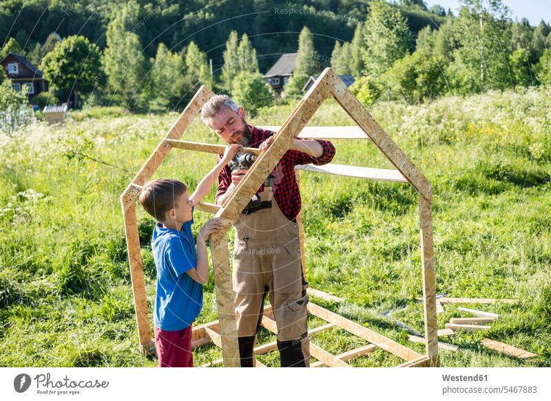 Boy helping carpenter to make playhouse on sunny day color image colour image outdoors location shots outdoor shot outdoor shots daylight shot daylight shots