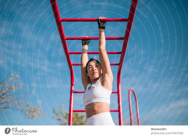 Confident sportswoman hanging on monkey bars while sports training in public park color image colour image outdoors location shots outdoor shot outdoor shots