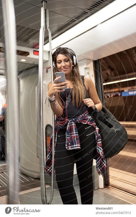 Portrait of smiling woman with guitar backpack and headphones looking at cell phone in underground train rucksacks backpacks back-packs Smartphone iPhone