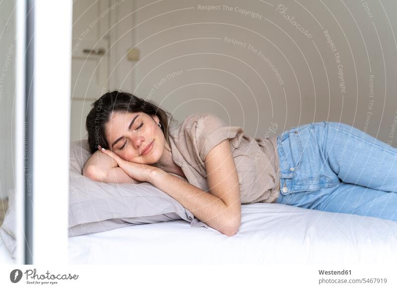 Smiling young woman lying on bed with closed eyes windows shirts pants Trouser Denim Jeans beds relax relaxing smile asleep relaxation delight enjoyment