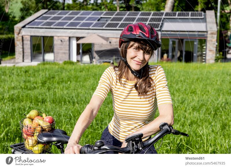 Portrait of smiling woman with bicycle and organic fruit on a meadow in front of a house human human being human beings humans person persons
