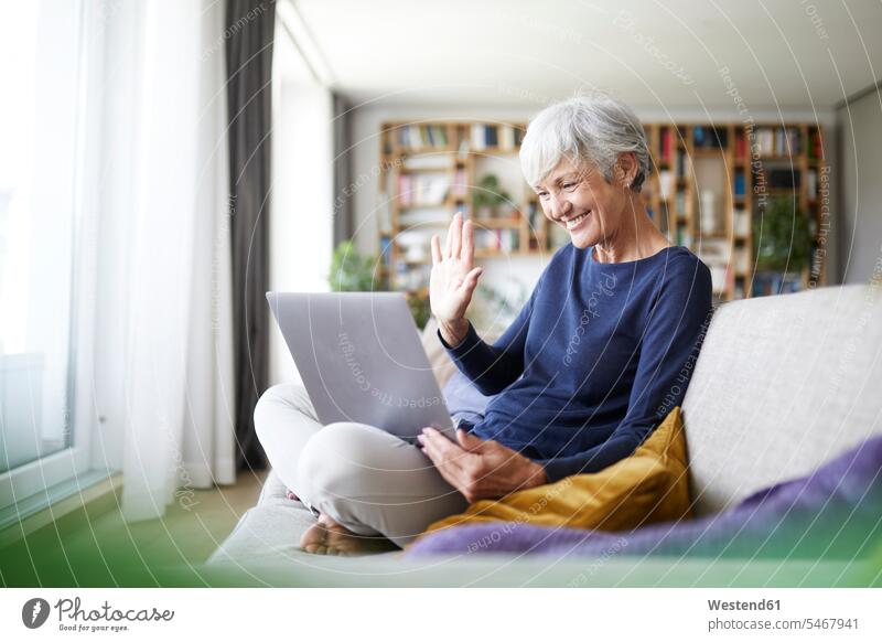 Senior woman doing high five on video call while using laptop at home color image colour image indoors indoor shot indoor shots interior interior view Interiors