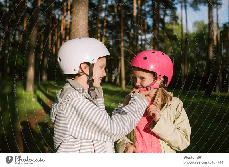 Happy boy fastening cycling helmet for girl in forest color image colour image outdoors location shots outdoor shot outdoor shots day daylight shot
