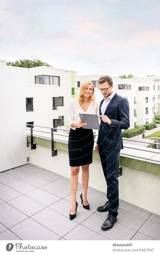 Real estate agent standing on a balcony with customer, looking at digital tablet businesswoman businesswomen business woman business women Businessman