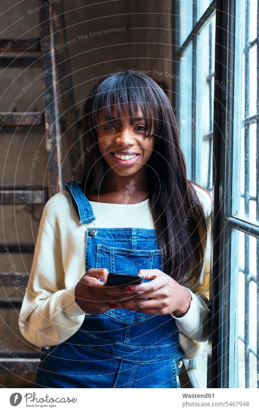 Portrait of laughing woman with cell phone leaning against window loft lofts females women portrait portraits using use windows Smartphone iPhone Smartphones