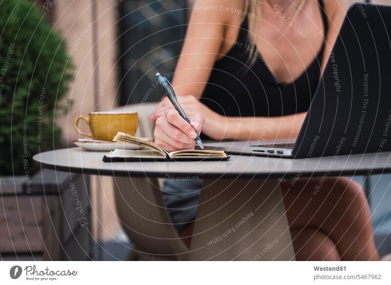 Young woman sitting on roof terrace taking notes, partial view females women memo notice Seated Adults grown-ups grownups adult people persons human being