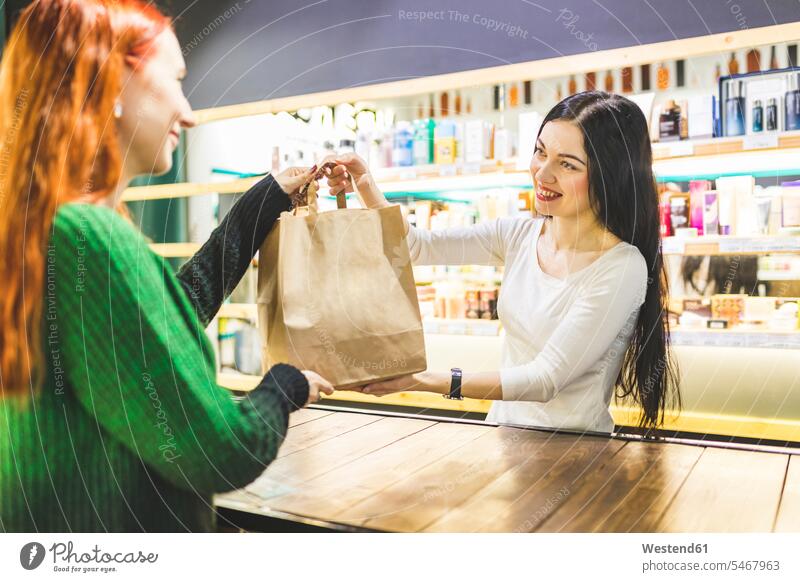 Smiling shop assistant handing over paper bag to customer in a cosmetics shop paper bags shop assistants giving give female customer smiling smile woman females