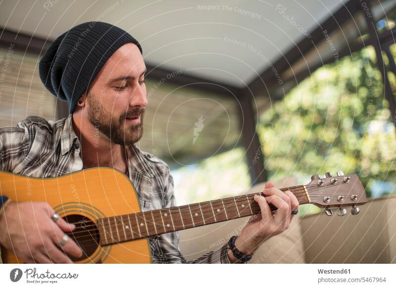 Young man at home sitting on couch playing guitar Seated music guitars settee sofa sofas couches settees making music playing music make music play music men