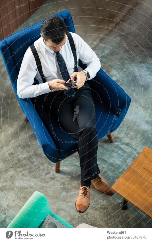 Top view of businessman sitting in blue armchair using smartphone Arm Chairs armchairs Seated Smartphone iPhone Smartphones Businessman Business man Businessmen