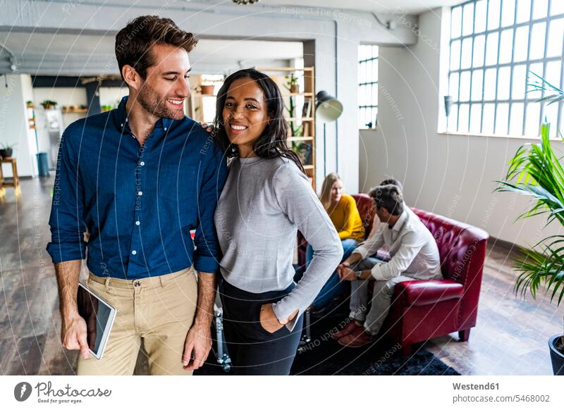 Portrait of smiling businessman and businesswoman with coworkers in background in loft office businesswomen business woman business women portrait portraits