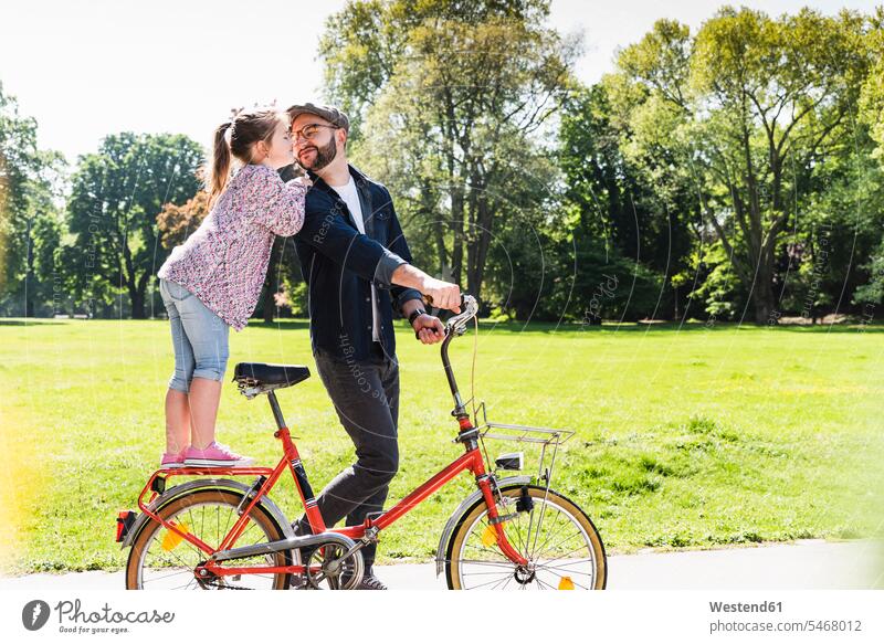 Daughter kissing father with bicycle in a park daughter daughters kisses bikes bicycles fathers daddy dads papa active parks child children family families