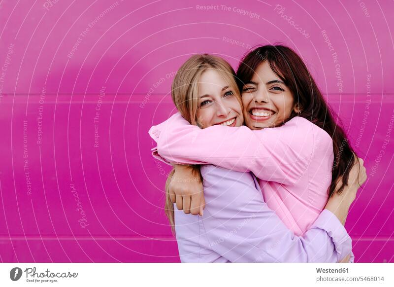 Happy sisters embracing each other against pink wall color image colour image outdoors location shots outdoor shot outdoor shots day daylight shot