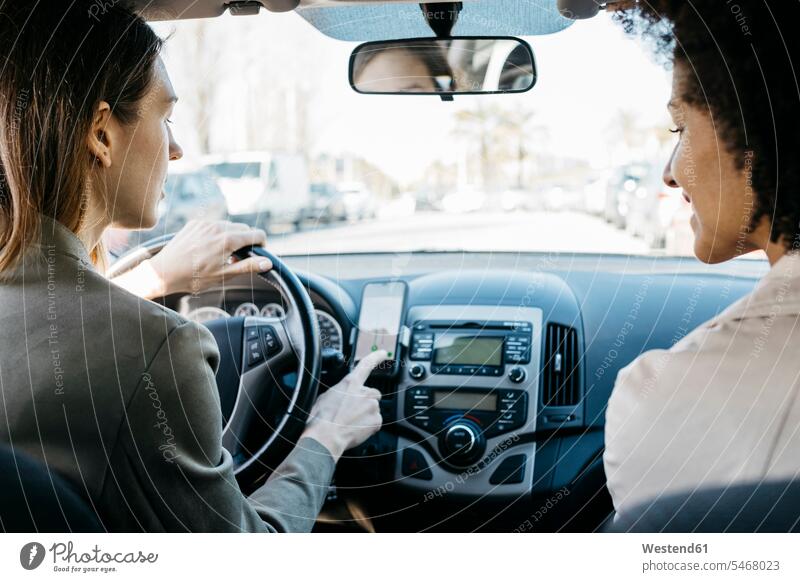 Two women driving in a car through the city using a telephone navigation app female friends application apps applications woman females town cities towns drive