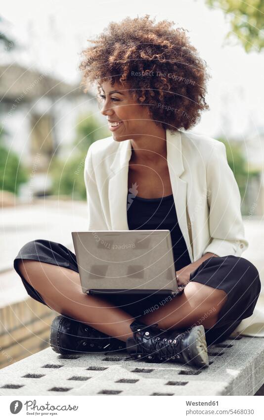 Fashionable young woman with curly hair sitting on bench with laptop laughing Seated Laptop Computers laptops notebook benches curls females women Laughter