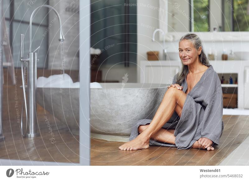 Smiling mature woman sitting by bathtub on floorboard in bathroom color image colour image outdoors location shots outdoor shot outdoor shots day daylight shot