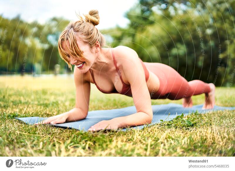 Athletic woman doing plank exercises outdoors in the park practising train training smile exercising practice practise delight enjoyment Pleasant pleasure