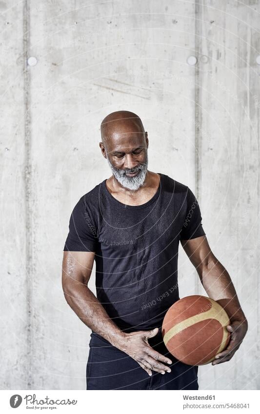 Mature man holding basketball at concrete wall Basketball men males concrete walls sport sports Adults grown-ups grownups adult people persons human being