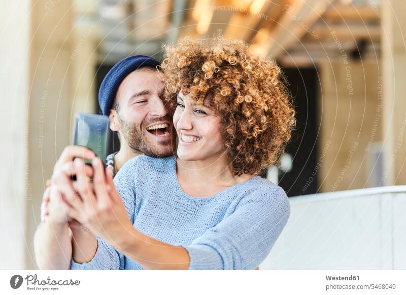 Laughing couple taking a selfie Germany casual beanie beanies stocking cap stocking caps stocking-cap Selfie Selfies Smartphone iPhone Smartphones self-portrait